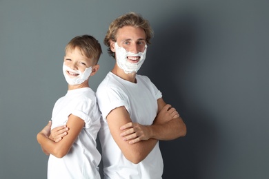 Photo of Father and son with shaving foam on faces against color background