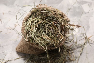 Dried hay in burlap sack on light grey textured table, above view