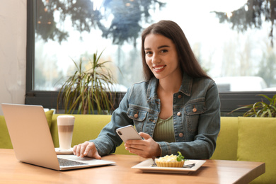 Photo of Young blogger with smartphone and laptop in cafe