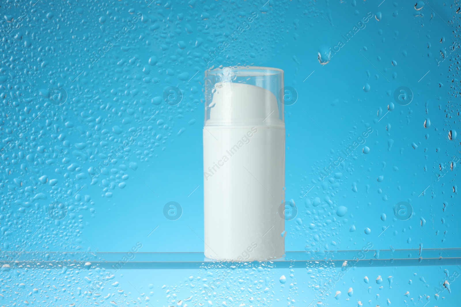 Photo of Bottle with moisturizing cream on light blue background, view through wet glass