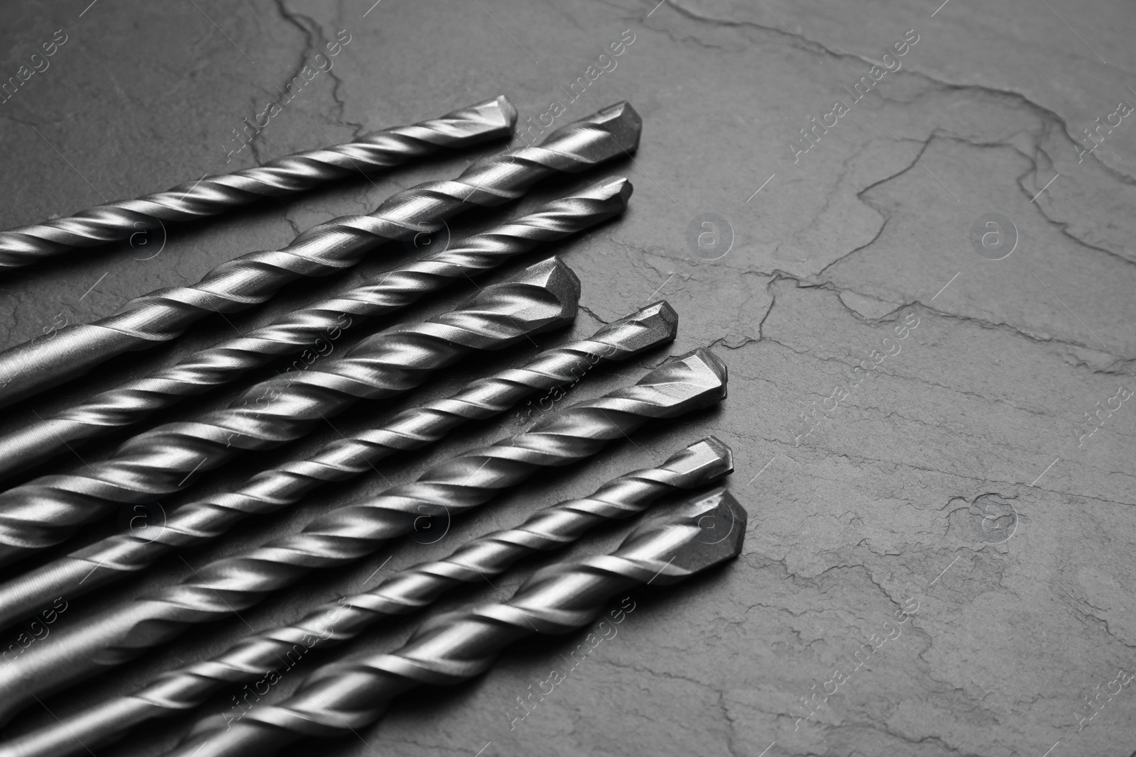 Photo of Different drill bits on black table, closeup. Space for text