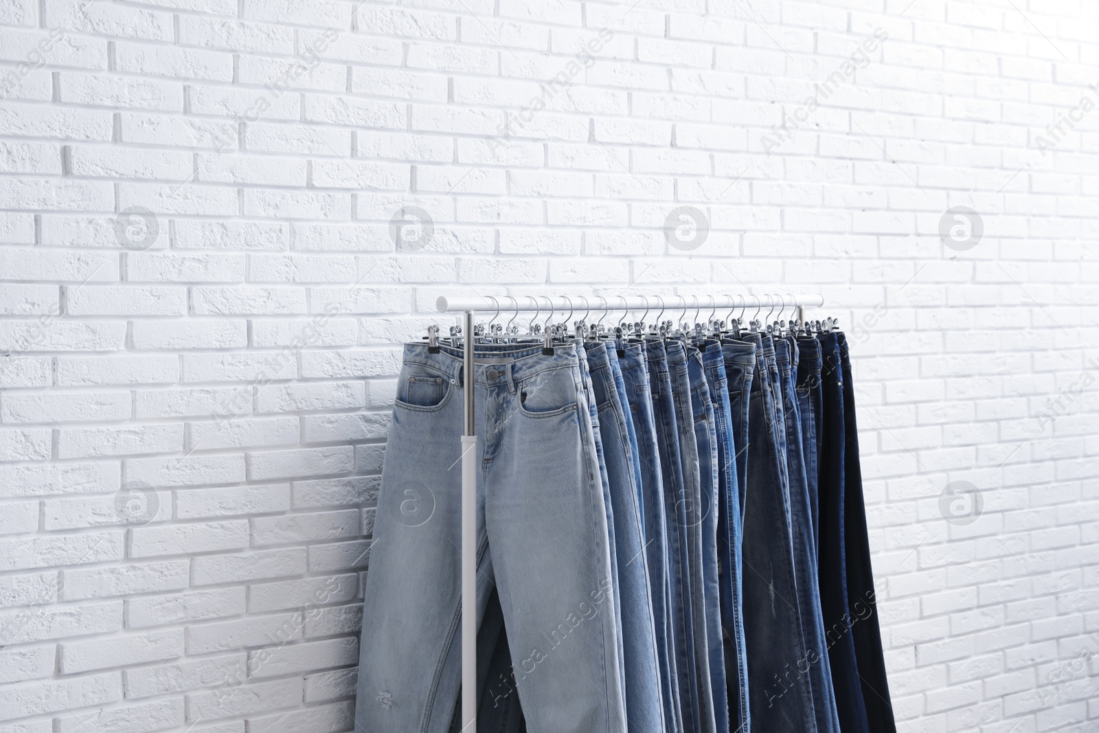 Photo of Rack with stylish jeans near brick wall