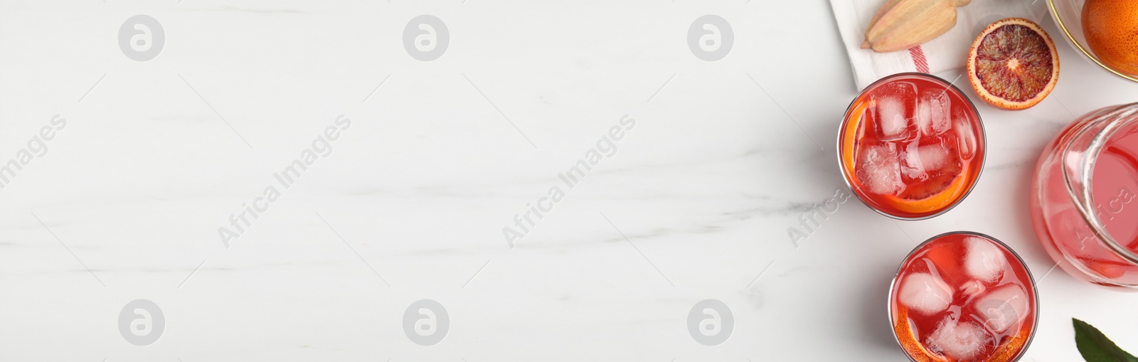 Image of Tasty sicilian orange juice with ice cubes, fruits and squeezer on white marble table, flat lay with pace for text