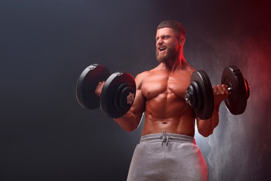 Emotional young bodybuilder exercising with dumbbells in smoke on color background, low angle view. Space for text