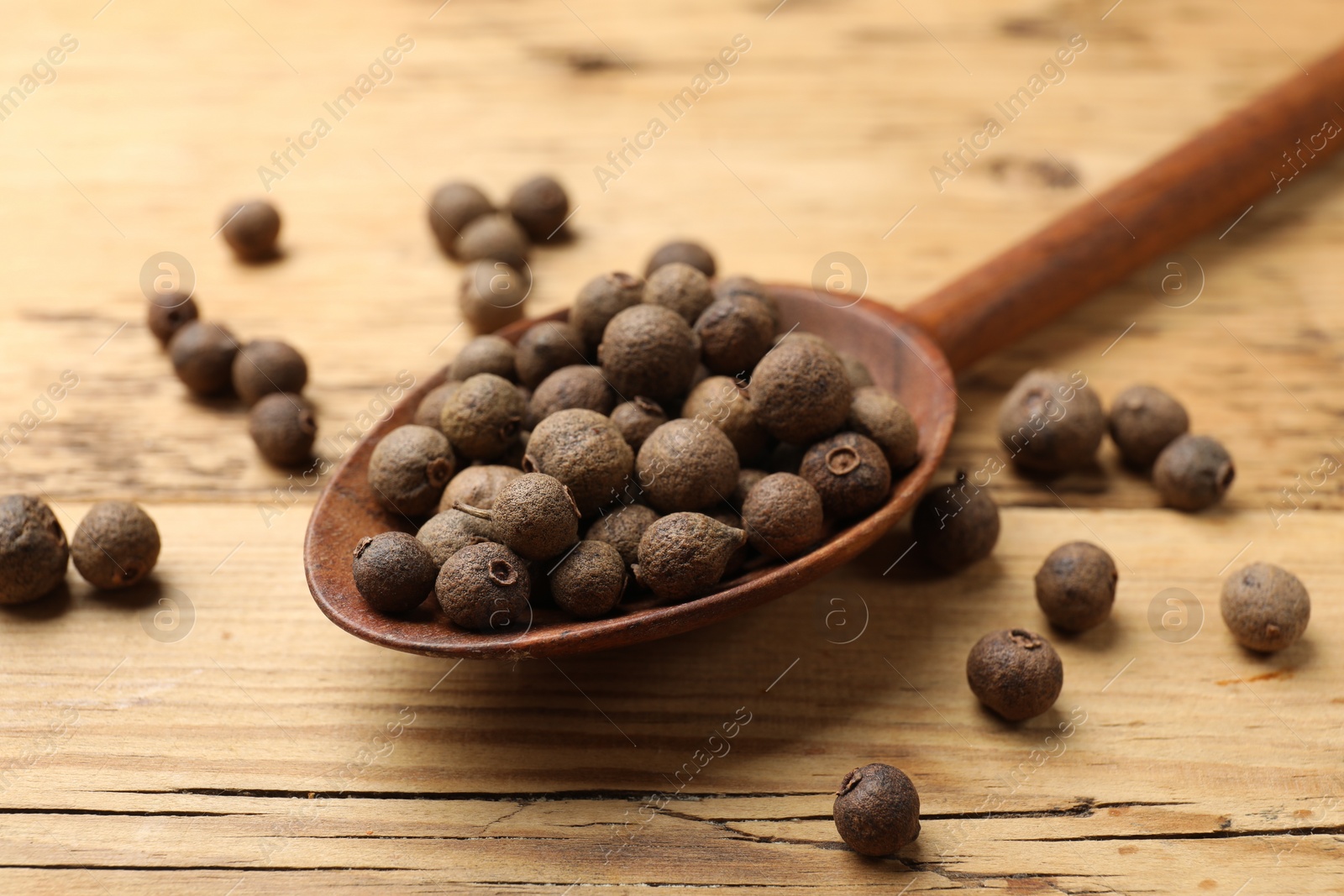 Photo of Dry allspice berries (Jamaica pepper) and spoon on wooden table, closeup