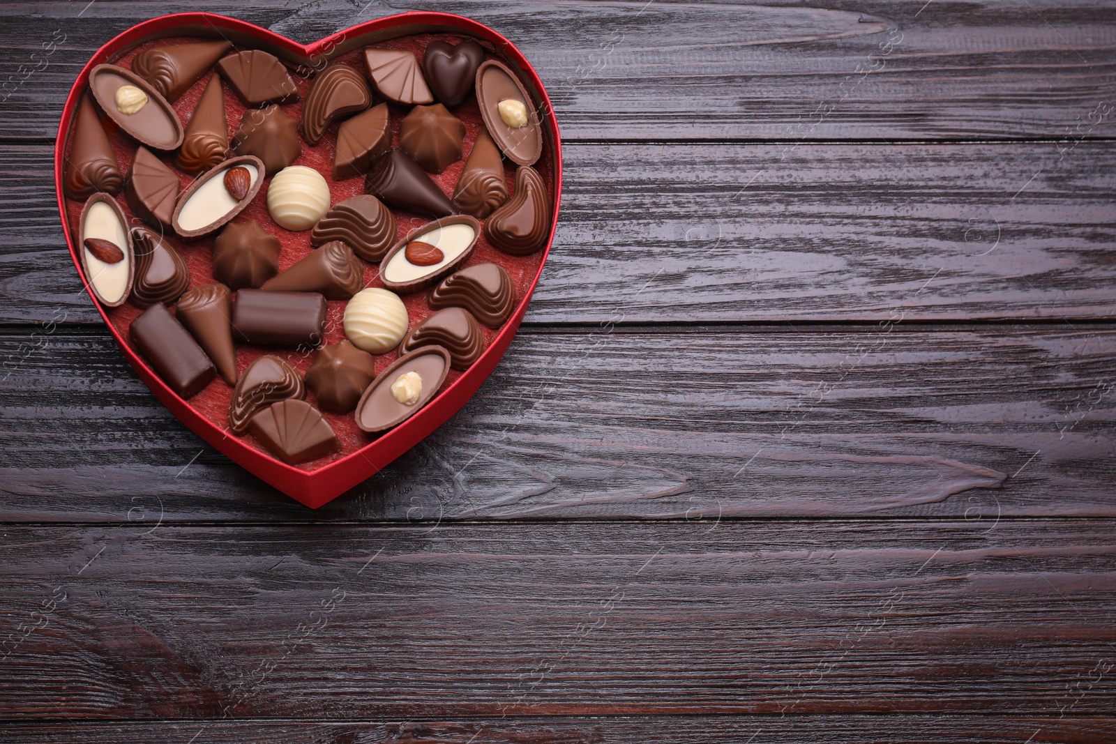 Photo of Heart shaped box with delicious chocolate candies on wooden table, top view. Space for text