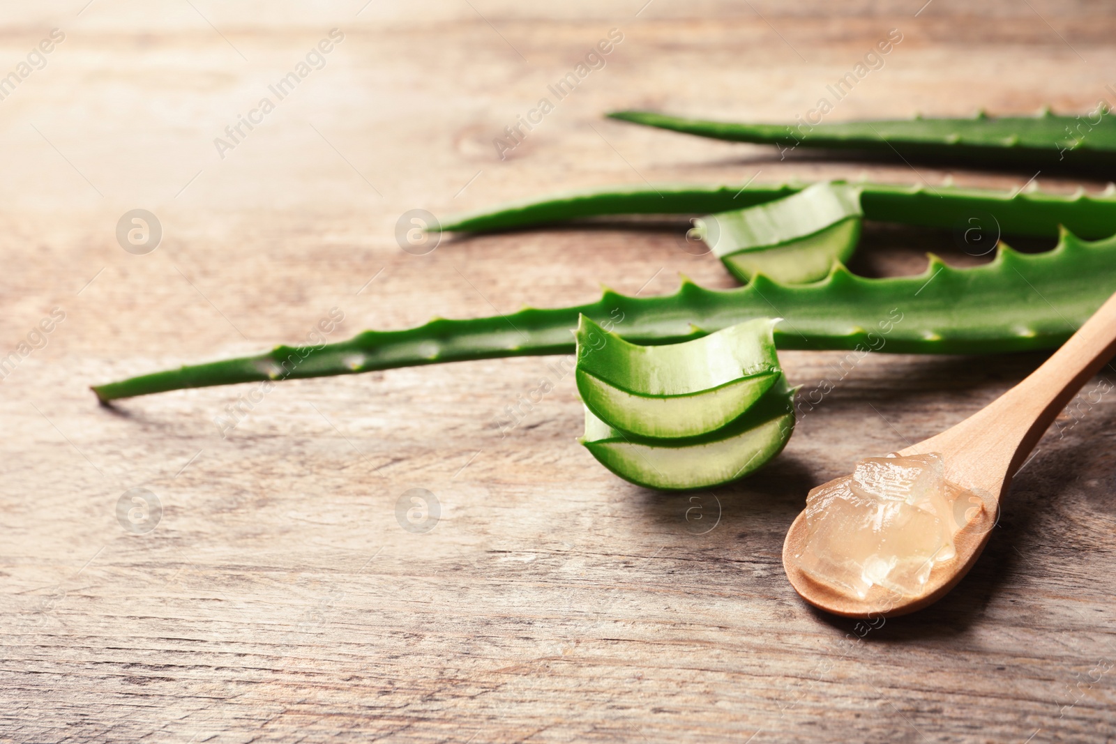 Photo of Spoon with aloe vera gel on wooden background. Space for text