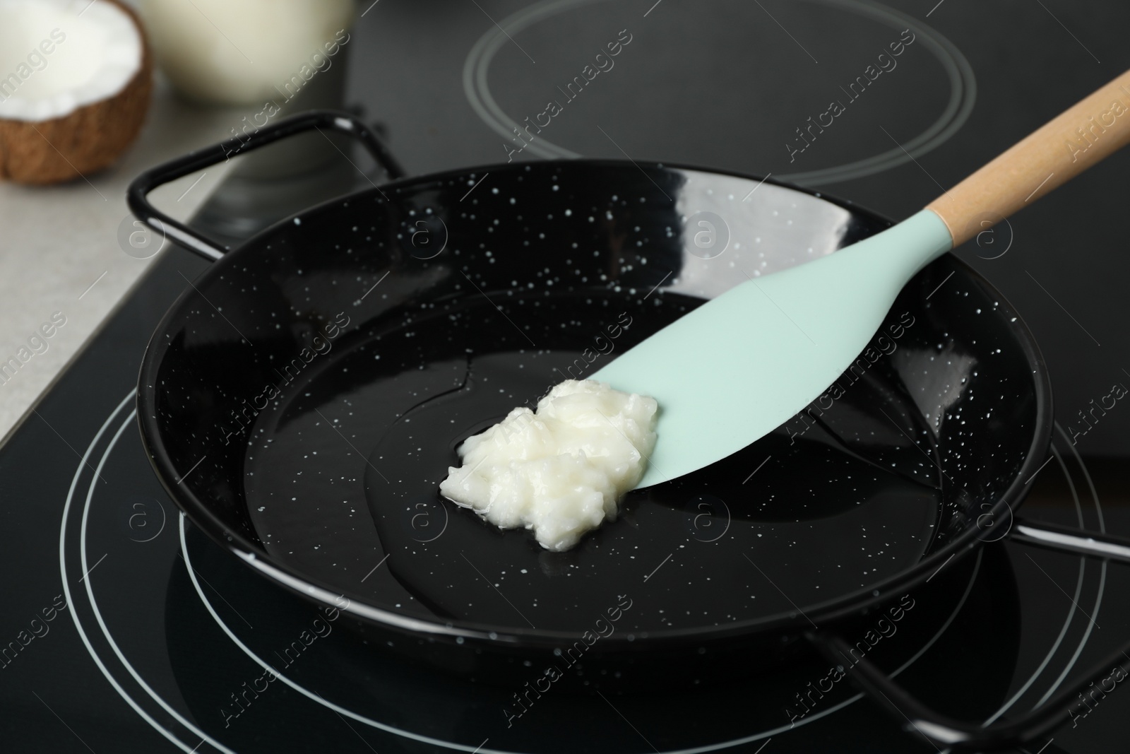 Photo of Frying pan with coconut oil and spatula on induction stove, closeup. Healthy cooking