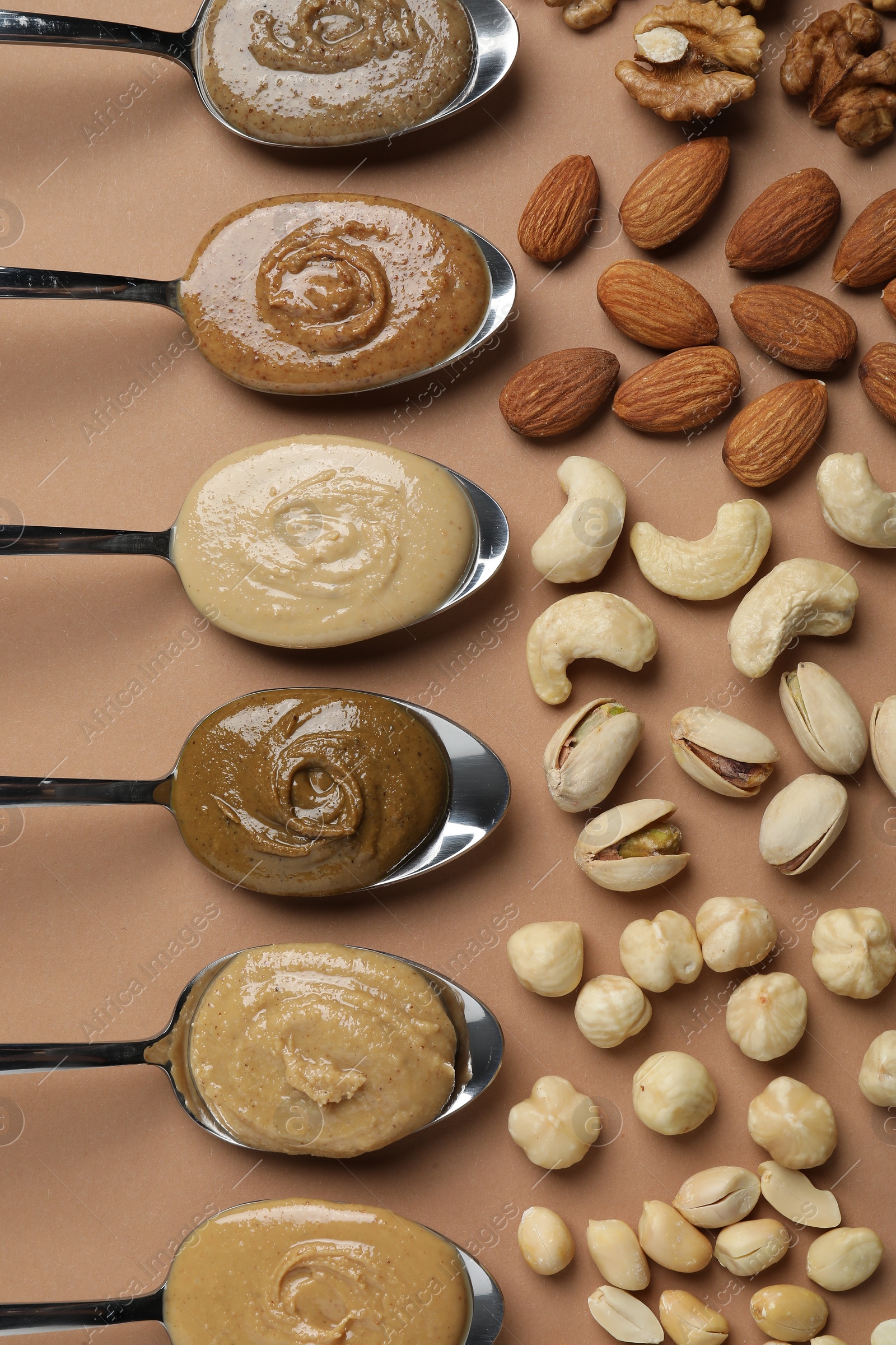 Photo of Tasty nut butters in spoons and raw nuts on light brown table, flat lay