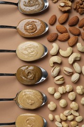 Tasty nut butters in spoons and raw nuts on light brown table, flat lay