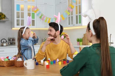 Photo of Family having fun while painting Easter eggs at table in kitchen