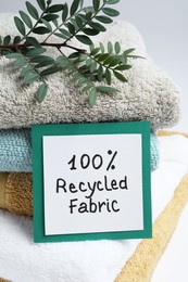 Photo of Recycling concept. Stacked towels and card with plant on white background, closeup