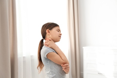 Photo of Little girl scratching neck indoors. Allergy symptoms