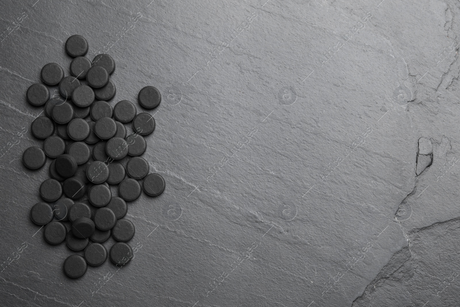 Photo of Pile of activated charcoal pills on black table, flat lay with space for text. Potent sorbent