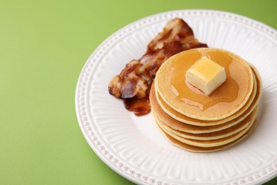 Photo of Delicious pancakes with butter, maple syrup and fried bacon on light green background