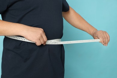 Man measuring waist with tape on light blue background, closeup