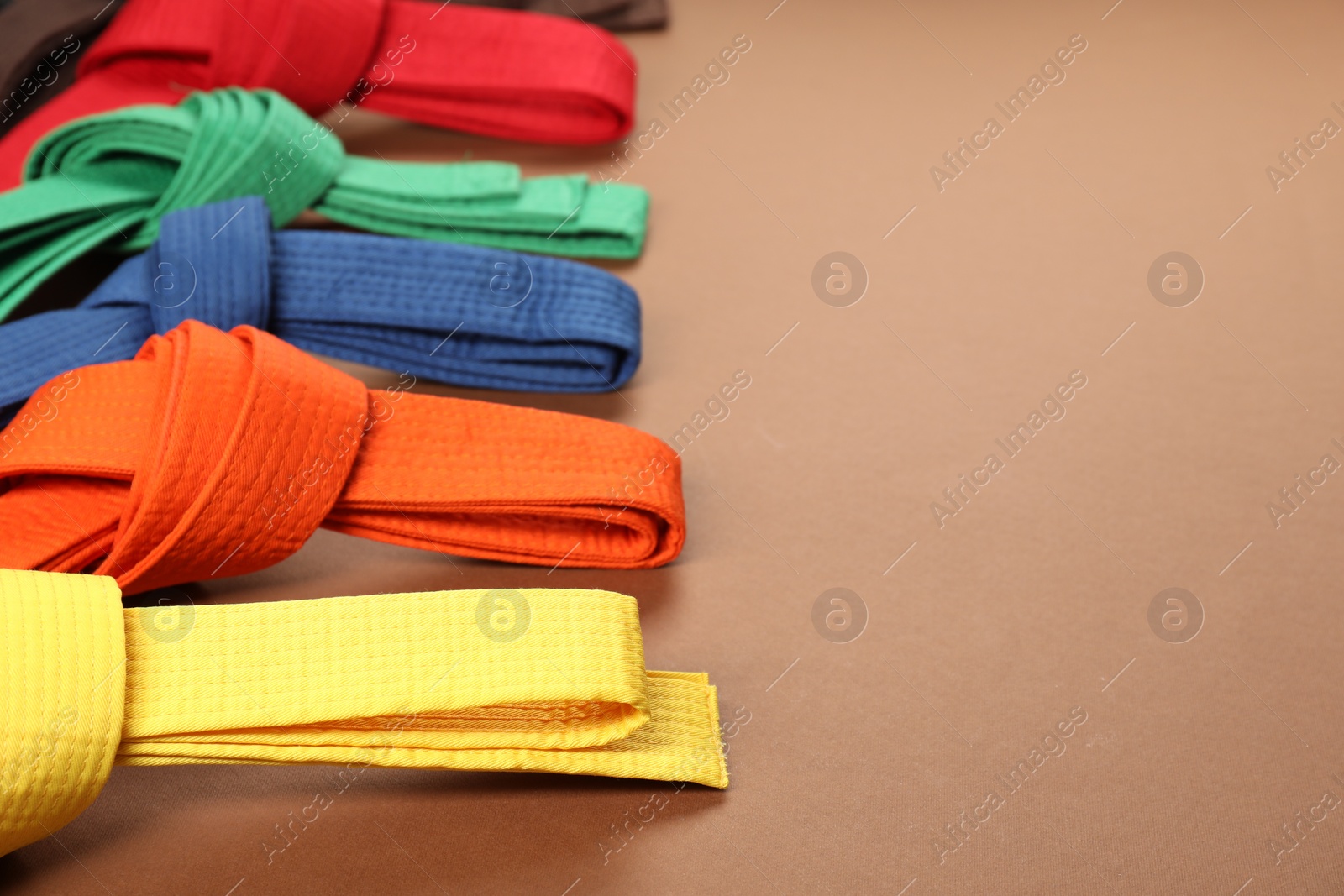 Photo of Colorful karate belts on brown background, closeup. Space for text