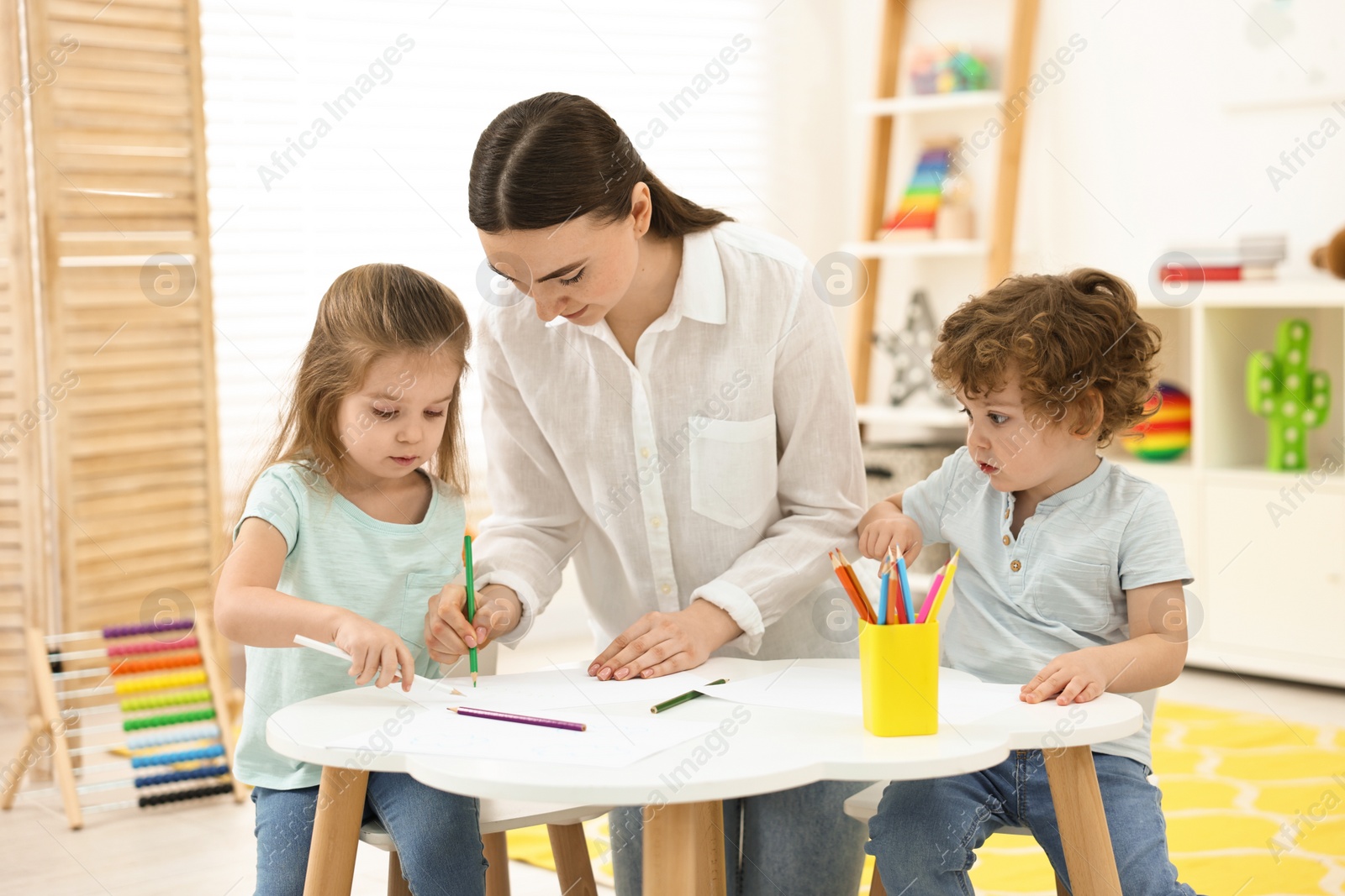 Photo of Mother and her little children drawing with colorful pencils at home