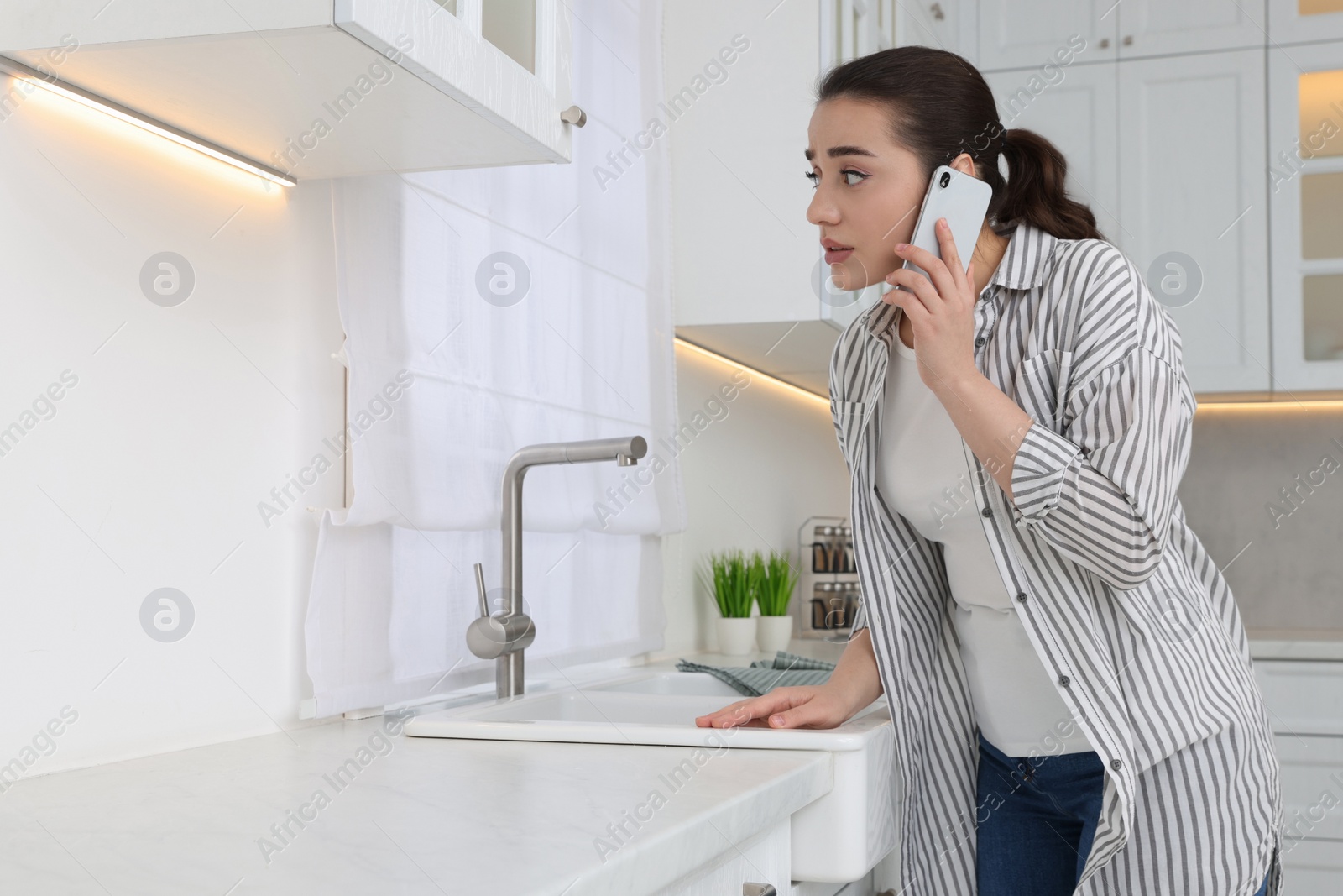 Photo of Woman talking on phone and looking at wall in kitchen