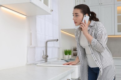 Photo of Woman talking on phone and looking at wall in kitchen