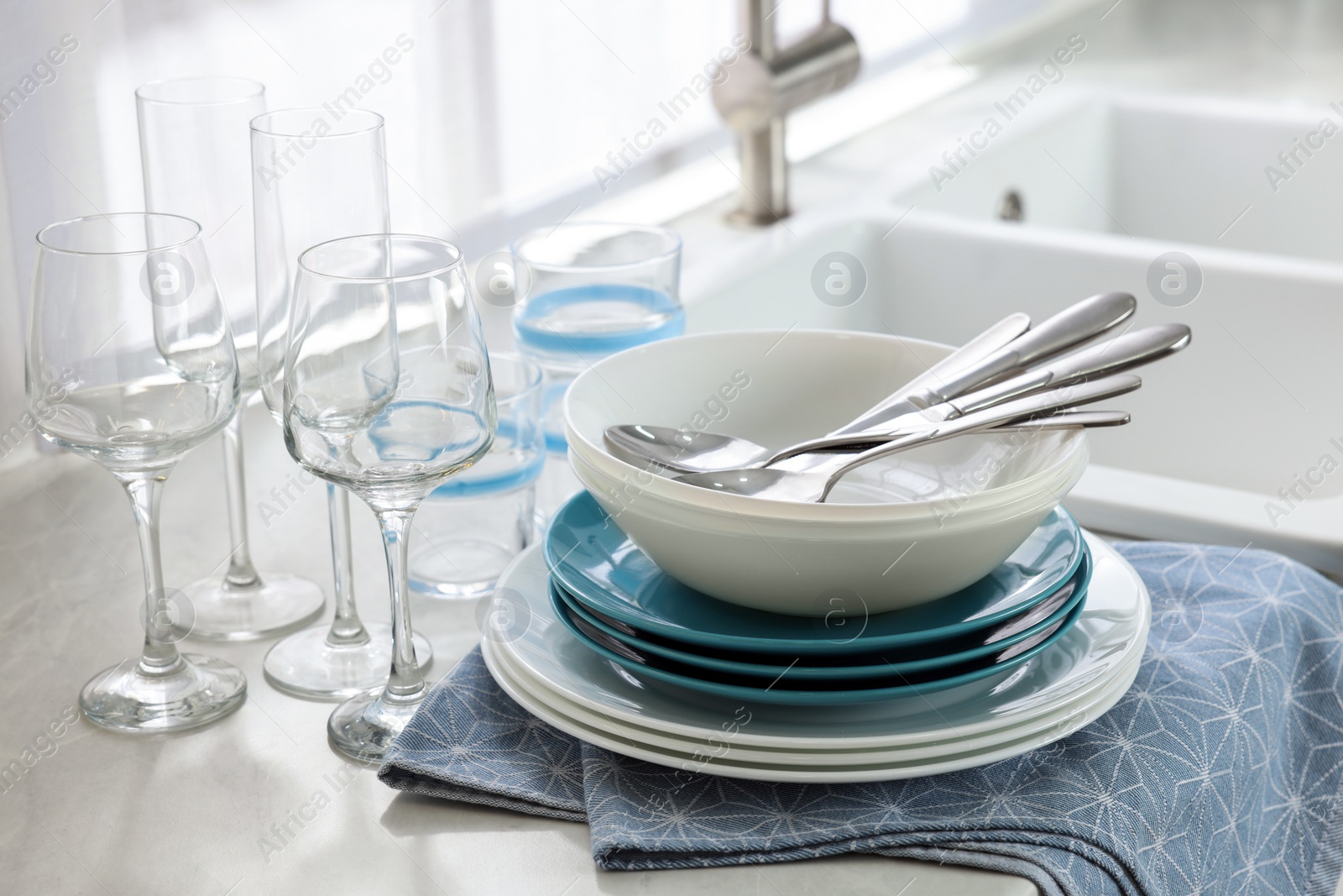 Photo of Different clean dishware, cutlery and glasses on countertop in kitchen