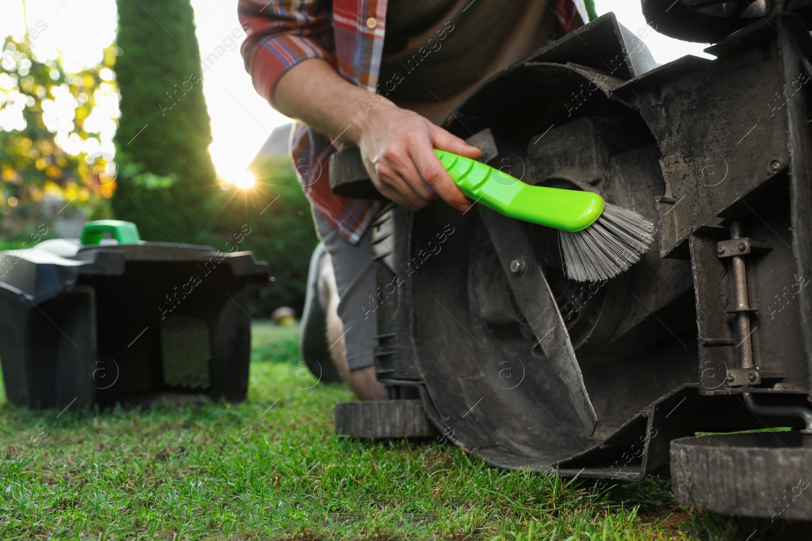 Photo of Man cleaning lawn mower with brush in garden, closeup