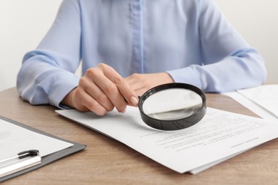 Woman looking at document through magnifier at wooden table, closeup. Searching concept