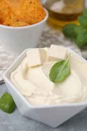 Photo of Delicious tofu sauce and basil leaves on grey table, closeup