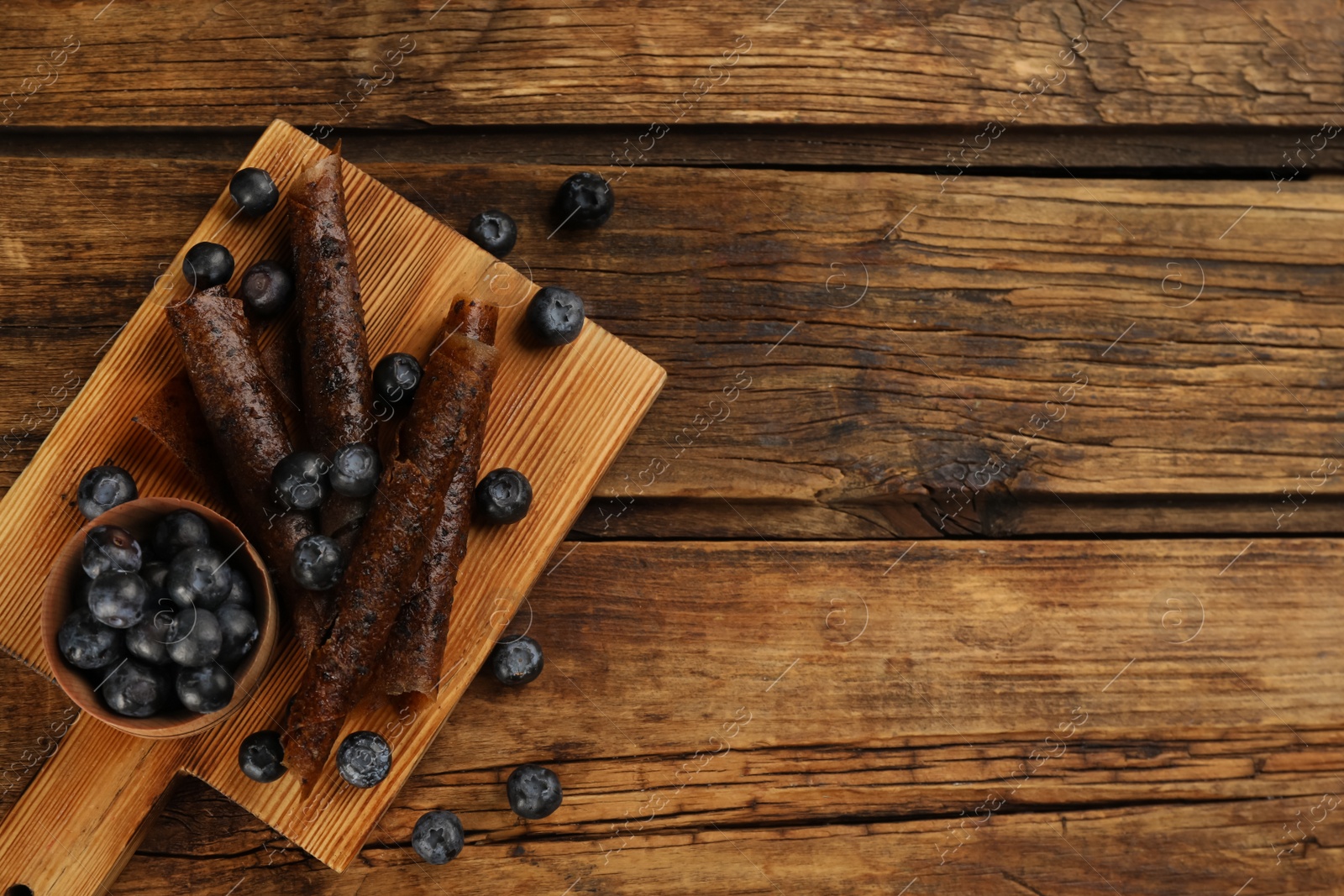 Photo of Delicious fruit leather rolls and blueberries on wooden table, flat lay. Space for text