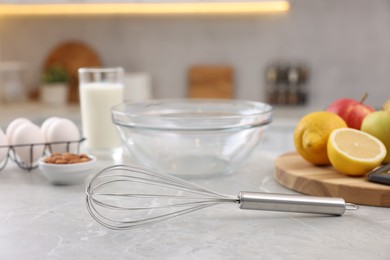 Metal whisk, bowl and different products on gray marble table in kitchen