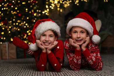 Photo of Happy children wearing Santa hats on floor at home
