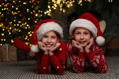 Happy children wearing Santa hats on floor at home