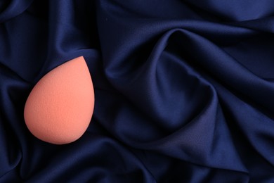 Beige makeup sponge on blue silk cloth, top view. Space for text