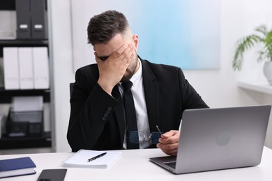 Overwhelmed man at table with laptop in office