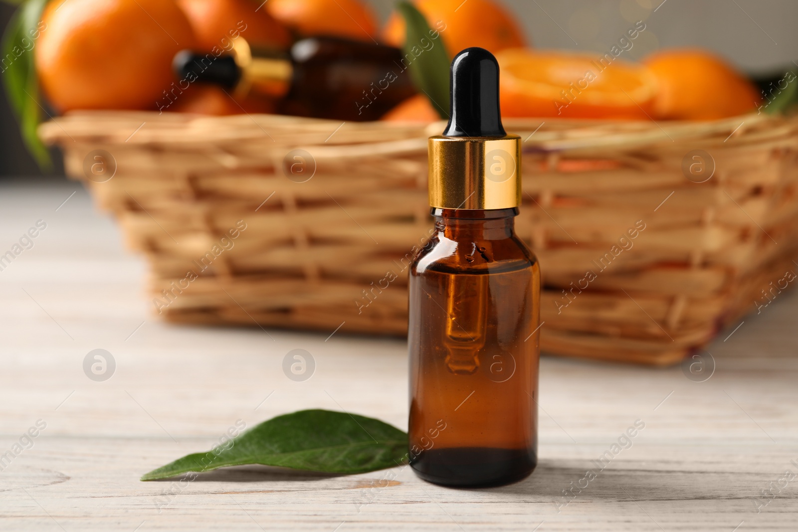 Photo of Bottle of tangerine essential oil and green leaf on white wooden table, closeup