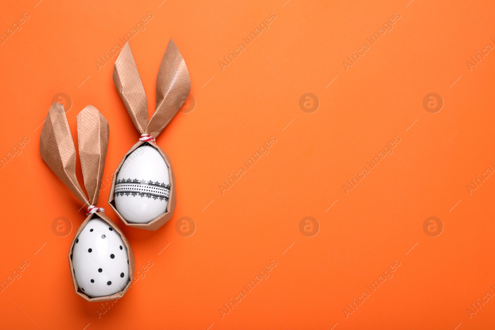 Photo of Easter bunnies made of craft paper and eggs on orange background, flat lay. Space for text