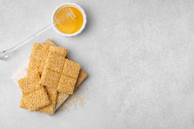 Delicious sesame kozinaki bars and honey on light grey table, flat lay. Space for text