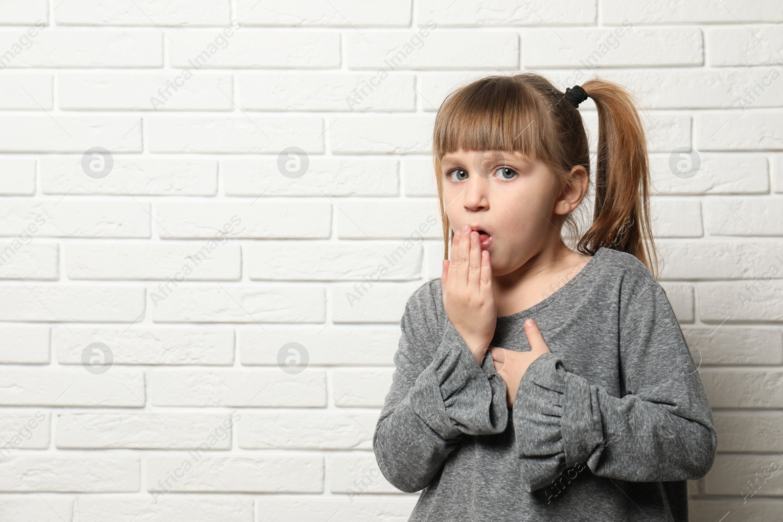 Photo of Cute little girl coughing near brick wall. Space for text