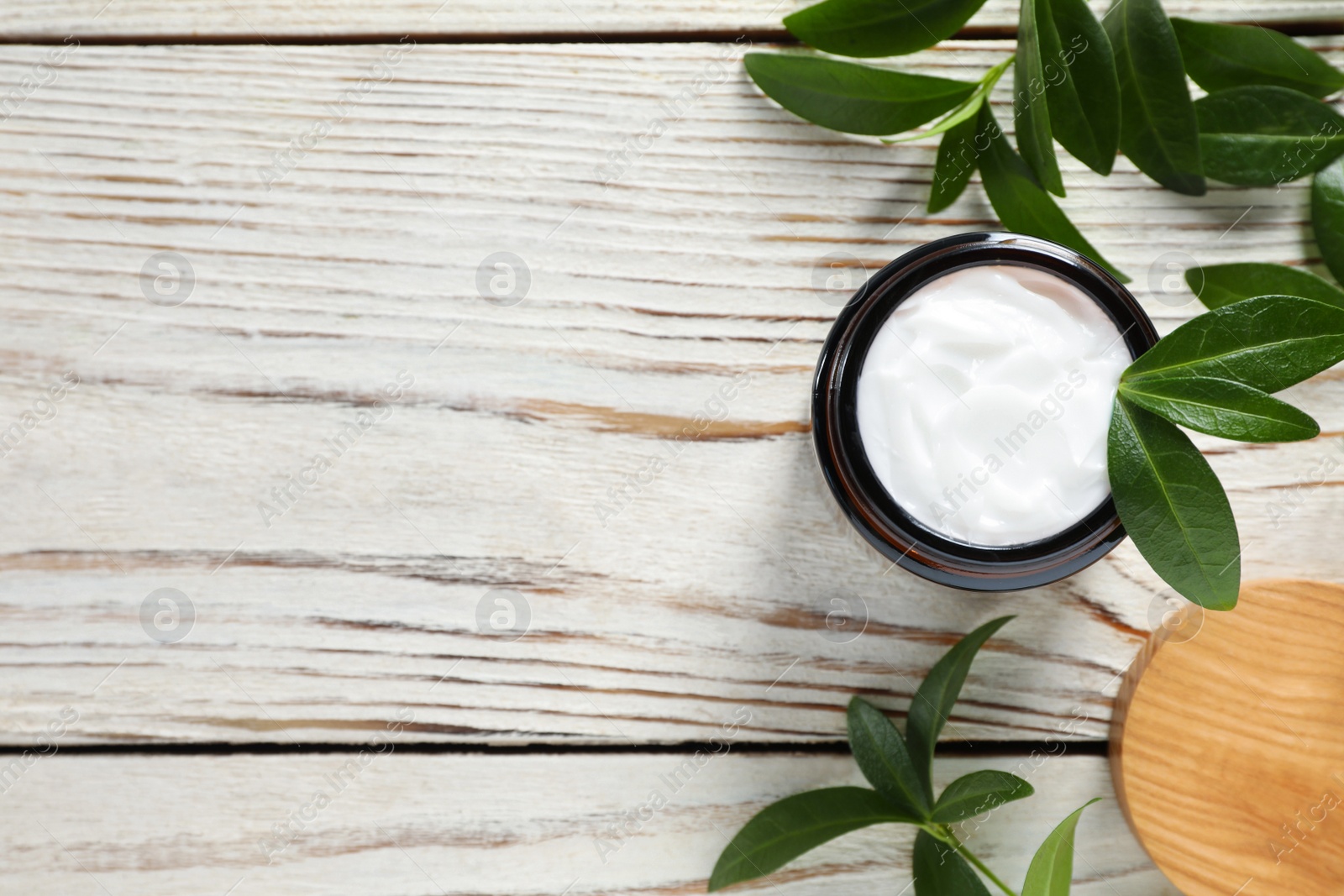 Photo of Jar of face cream and green leaves on wooden table, flat lay. Space for text