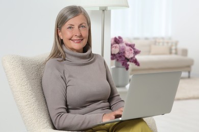 Photo of Beautiful senior woman using laptop in armchair at home