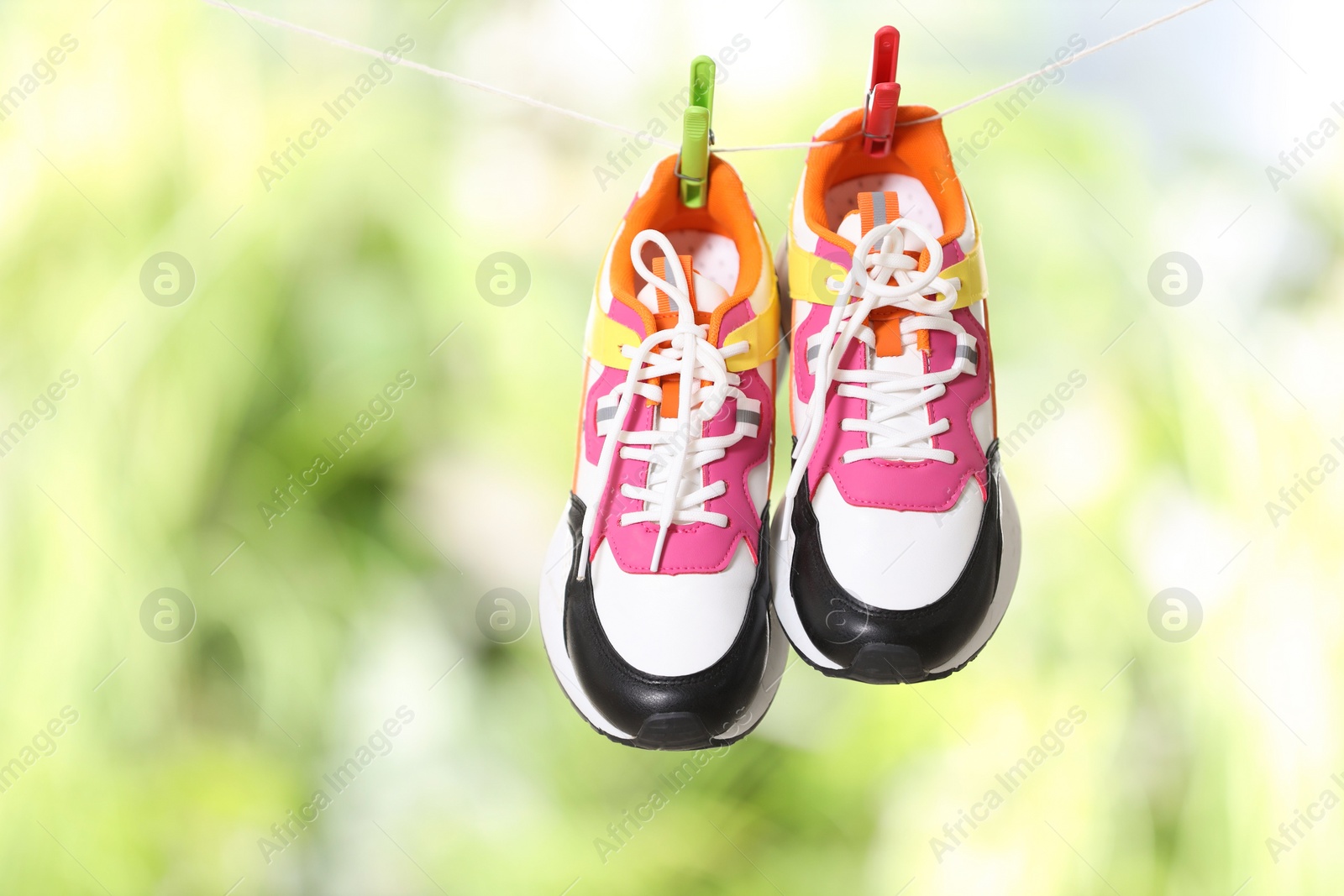 Photo of Stylish sneakers drying on washing line against blurred background