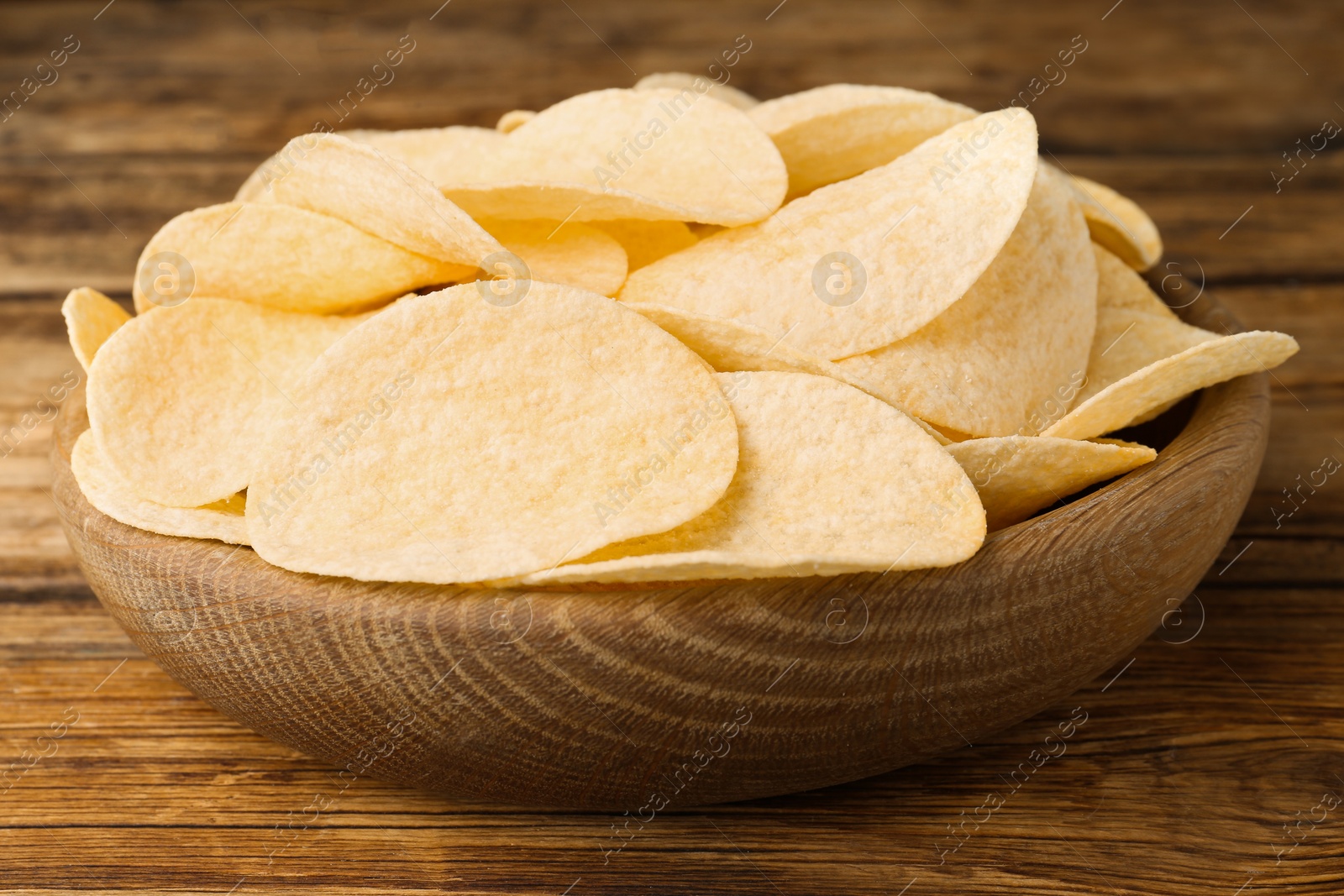 Photo of Bowl with delicious potato chips on wooden table, closeup