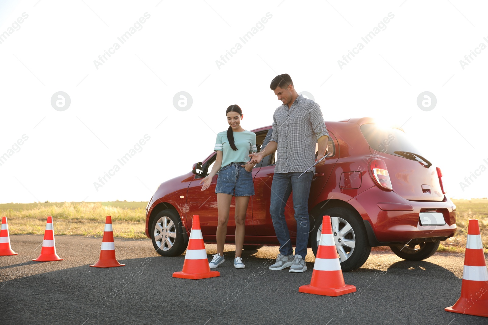 Photo of Instructor with clipboard near car and his student outdoors. Driving school exam