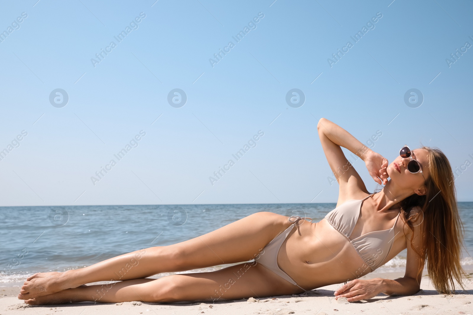 Photo of Attractive woman with perfect body in bikini lying on sandy beach near sea