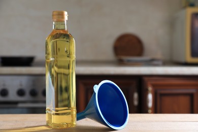 Photo of Bottle of cooking oil and funnel on wooden table in kitchen