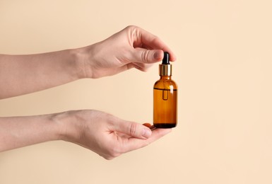 Photo of Woman holding bottle of cosmetic oil on beige background, closeup