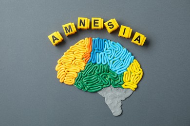 Photo of Word Amnesia and brain with sections made of plasticine on grey background, flat lay