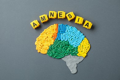 Word Amnesia and brain with sections made of plasticine on grey background, flat lay