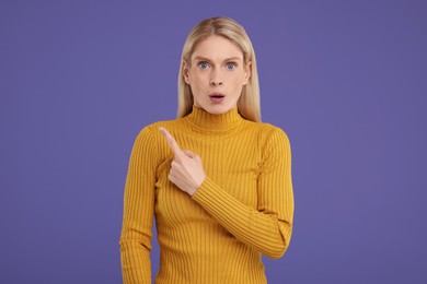 Surprised woman pointing at something on violet background, space for text