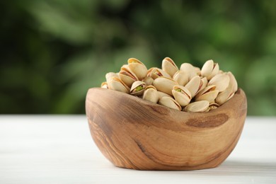 Photo of Tasty pistachios in bowl on white table against blurred background. Space for text